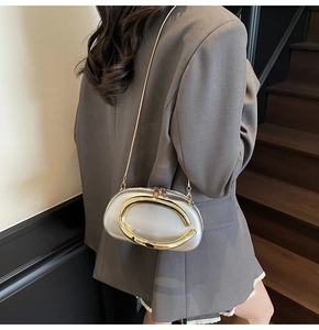 Silver oval evening bag featuring a prominent gold C-shaped metal handle and slim chain strap