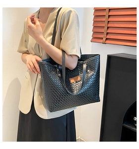 Close-up of black woven tote bag with brown leather logo detail and shoulder straps
