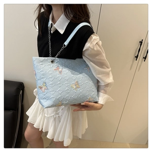 Detail of light blue tote bag featuring colorful butterfly embroidery and metal chain strap