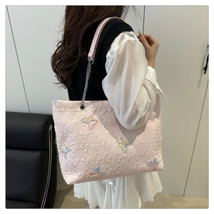 Detailed shot of a pink quilted tote bag with butterfly embroidery and silver chain straps