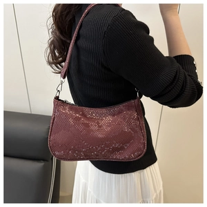 Detail of burgundy snakeskin baguette bag worn by model over a black sweater