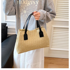 Close-up of a stylish woven straw basket handbag with black handles held by a model.