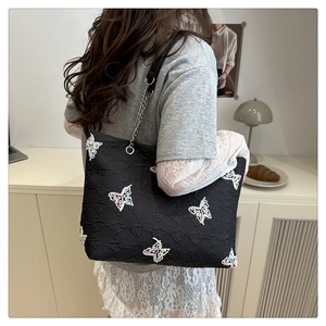 Detail of black tote bag featuring colorful butterfly embroidery and silver chain strap