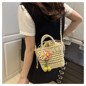 Detail of hand-woven straw bag with floral accents and drawstring liner on model