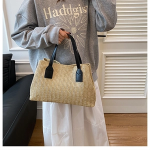 Casual hand-woven straw tote bag with black handles held by a model in lifestyle setting