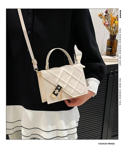 Detail of quilted white crossbody bag with black gold lock and adjustable strap