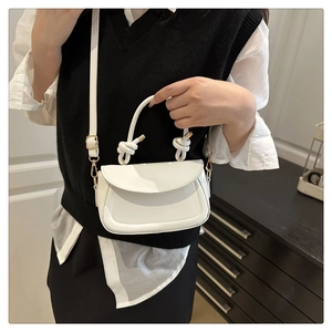 Detail of white leather handbag featuring elegant curved stitching and decorative handle knots