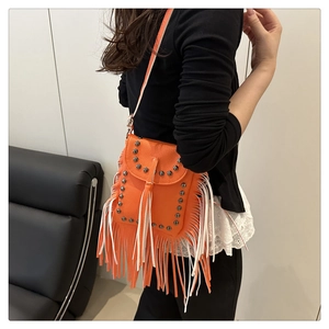 Primer plano del bolso bandolera de cuero naranja con remaches metálicos y flecos