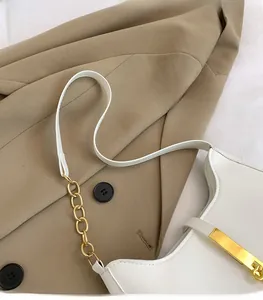 Dettaglio borsa a spalla in pelle bianca con finiture dorate su giacca kaki