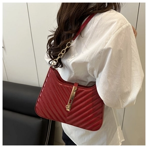 Close-up of red patent leather shoulder bag with V-shaped quilting and gold metal buckle