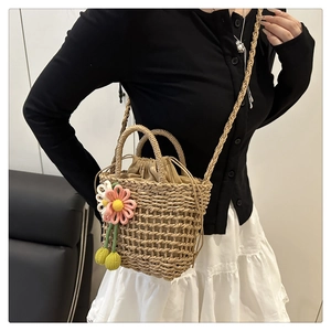 Detail of hand-woven straw bucket bag with floral charm and drawstring silk lining