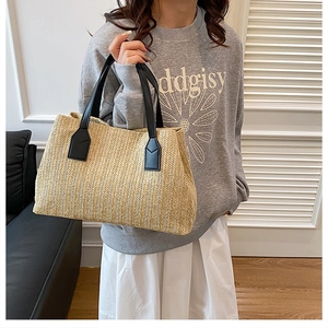 Stylish hand-woven straw tote bag with contrasting black handles, perfect for beach trips.