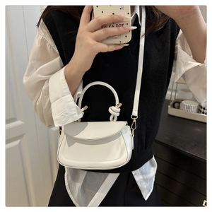 Detail of white mini crossbody bag with twisted top handle and golden hardware