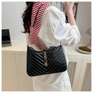 Detail of black quilted shoulder bag featuring V-shaped stitching and gold chain strap