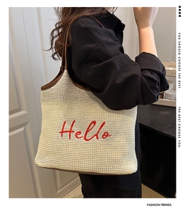 Detail of cream woven tote bag featuring red Hello embroidery and brown leather straps
