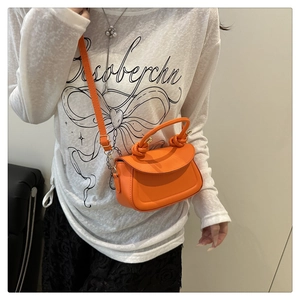 Close-up of orange mini leather crossbody bag with decorative knot handle and shoulder strap