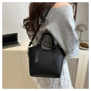 Litchi pattern black bucket bag shown as a crossbody on a model in a stylish indoor setting