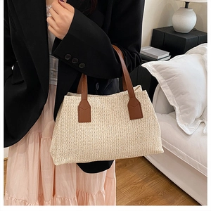 Elegant woven straw handbag with brown leather handles shown in a lifestyle indoor setting