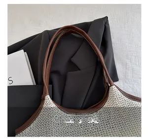 Detail of woven tote bag featuring brown leather handles with fine contrast stitching