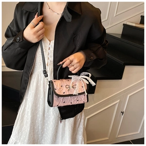 Detail of pink pleated handbag featuring lace bow, pearl accents and black bow patterns
