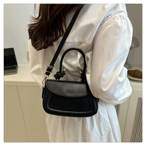 Close-up of black crossbody bag with knot handle and gold hardware on model in white dress