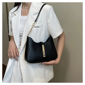Dettaglio della borsa in pelle nera con catena dorata su un blazer bianco