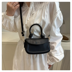 Detail of minimalist black crossbody bag with knotted handle and golden hardware on a model