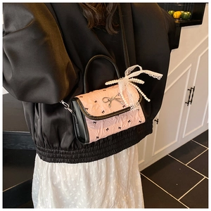 Detail of pink pleated handbag with black bows and pearl lace charm on a model