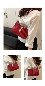 Detail of red quilted underarm bag with gold lock and chain strap on a white shirt