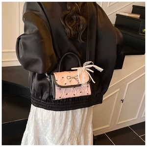Detail of pink ruffled crossbody bag with black bows and pearl lace on a model back