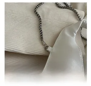Detail of silver box chain connector on a white textured minimalist shoulder handbag