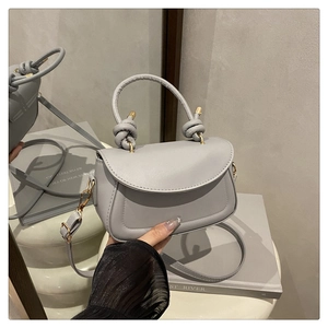 Detail of grey matte leather handbag featuring a knotted handle and golden metal buckle