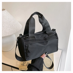 Détail du sac cylindrique noir en nylon avec poche zippée et pendentif triangulaire