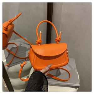 Close-up of bright orange crossbody bag featuring a unique knotted handle and gold hardware