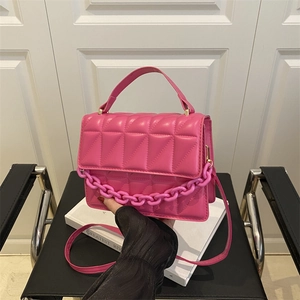 Sac bandoulière rose matelassé avec chaîne et poignée supérieure sur une chaise noire