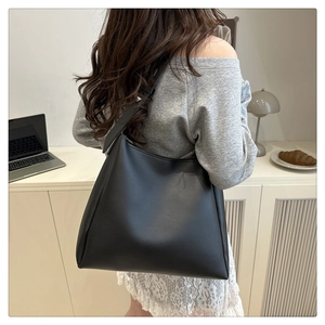 Minimalist large black leather tote bag worn by a model in a cozy, stylish room setting