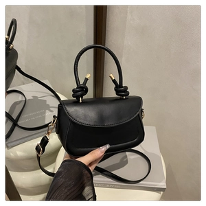 Detail of black leather handbag with unique knotted handle and elegant gold hardware accents