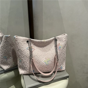 Pink quilted tote bag with butterfly embroidery and silver chain strap on a white stool