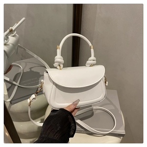 Close-up of white leather handbag featuring knotted handle and gold metal ring buckle detail