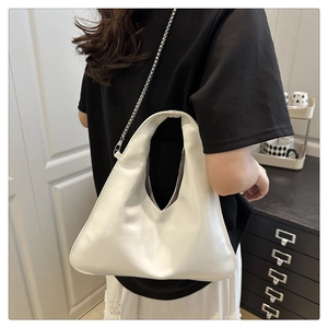 Close-up of a white leather crossbody bag with silver chain strap worn by a model
