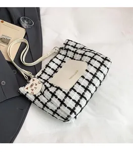 Detail of checkered tote bag with leather strap, cat charm and brand label on front