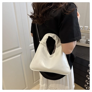 Detail view of a white glossy chain handbag shown on a shoulder in a modern setting