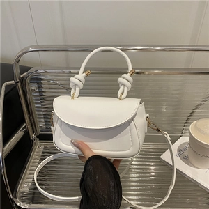 Elegant off-white crossbody bag with unique knot ring handle and slim shoulder strap