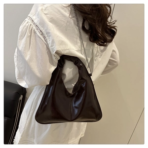 Detail of dark brown patent leather handbag with pleated handle and metallic chain strap