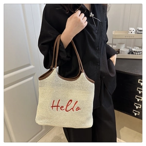 Detail of woven beach tote featuring red Hello embroidery and brown leather handle
