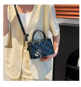 Detail of a black quilted crossbody bag featuring a metal lock and gold chain strap