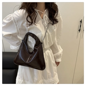 Detail of dark brown glossy shoulder bag with round handle and gold chain strap