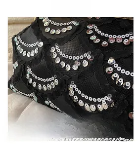Macro view of black mesh fabric with wavy silver sequins and delicate lace trim detail