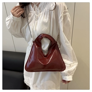 Glossy burgundy red mini bucket bag with chain strap held by a model in a white dress