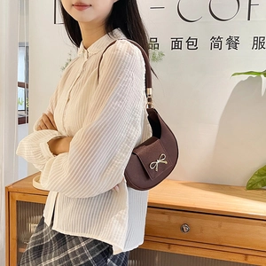Vista dettagliata della borsa a spalla a mezzaluna marrone con fiocco dorato su modella